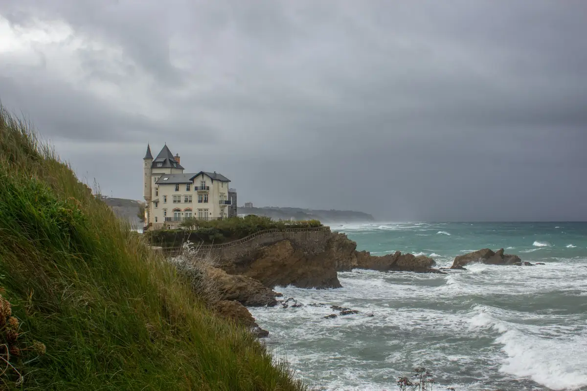 Una casa en lo alto de un acantilado, con el mar revuelto y el cielo gris